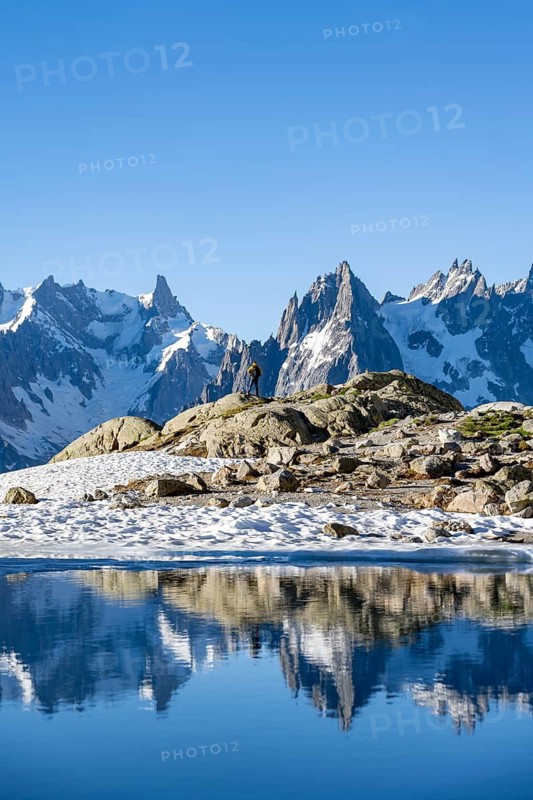 Young man in front of impressive mountain landscape in morning light, reflection in the Lac Blanc mountain lake, mountain summit, Aiguille Verte, Grandes Jorasses, Aiguille du Moine, Mont Blanc, Mont Blanc Massif, Chamonix-Mont-Blanc, Haute-Savoie, France