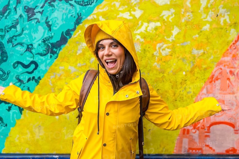 Young woman smiling with open arms, enjoying urban street art and vibrant colors while exploring the city during travel, expressing happiness and freedom