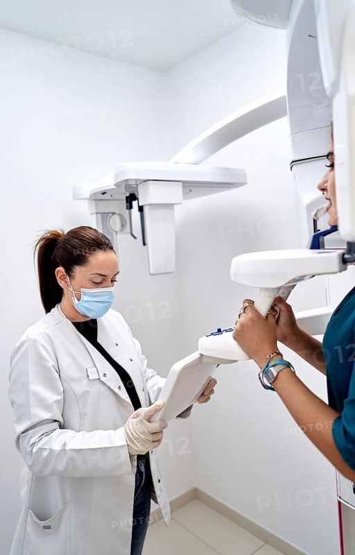 A dental assistant wearing protective gear operates an X-ray machine in a modern dental clinic, assisting a patient during a routine dental check-up for diagnostic imaging
