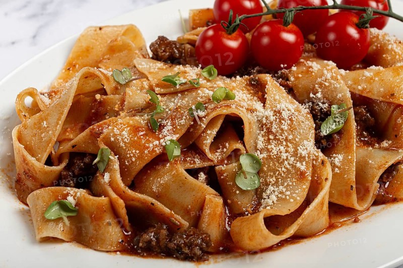 Pappardelle pasta with bolognese sauce, topped with parmesan cheese and cherry branch, homemade, no people