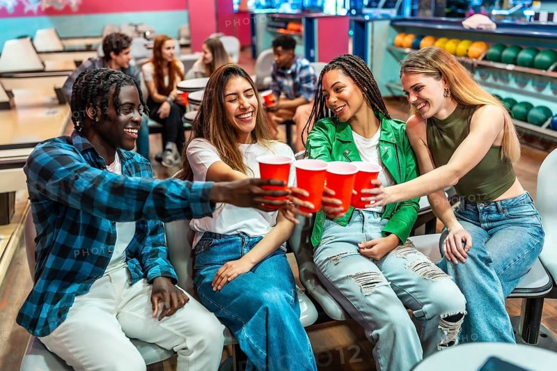 Group of cheerful young multiethnic friends toasting with red cups while enjoying a fun filled weekend at the bowling alley