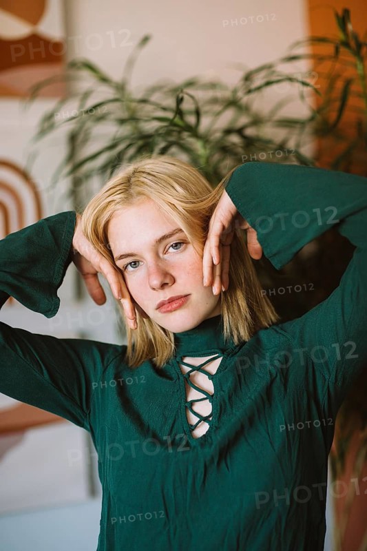 A thoughtful portrait of a teenager in a stylish green top, posing with hands near face. Natural backdrop enhances the serene and introspective mood