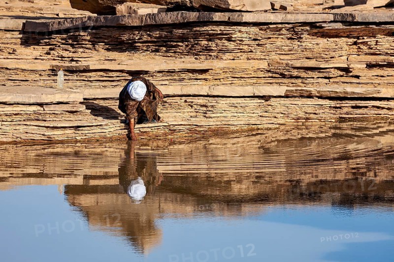Individual person scooping water from a rock with a reflective surface, Tuareg collecting water in the Sahara in Algeria