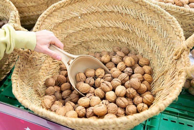 Cropped unrecognizable hands woman in a supermarket carefully selects fresh hazelnuts using a plastic scoop from a large wicker basket