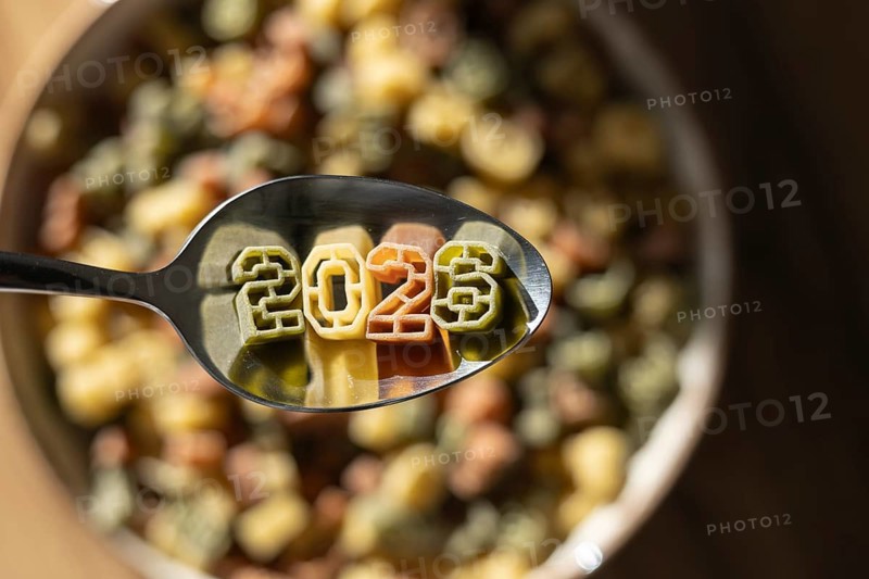 A spoonful of numerically shaped pasta displays the year 2026 above a bowl full of colorful number pasta, symbolizing new year celebrations