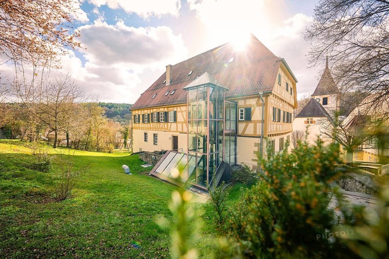 Timbered house with sunshine in the background, surrounded by a green garden and trees, Deufringen Castle, Aidlingen, Böblingen District, Germany