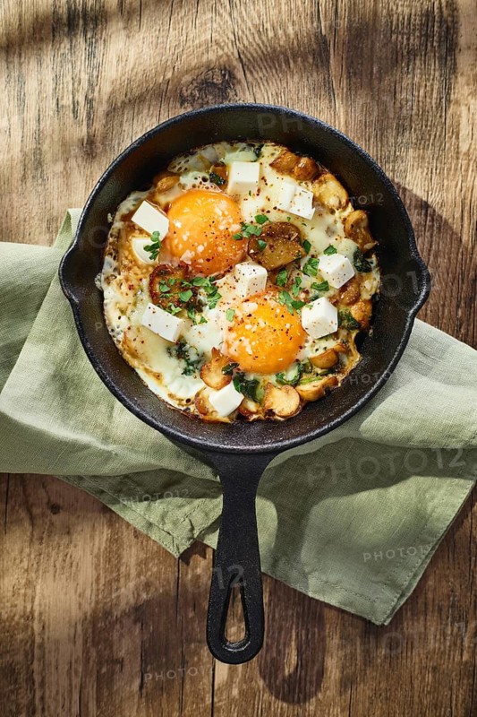 Fried eggs with spinach, mushrooms, grated cheese and feta cheese in small cast iron skillet. Top view