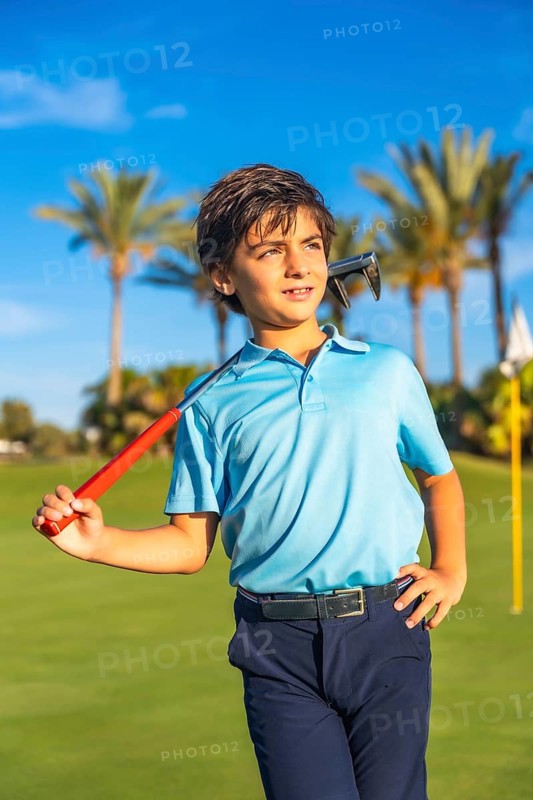 Vertical photo of a caucasian boy carrying a gold club along a course