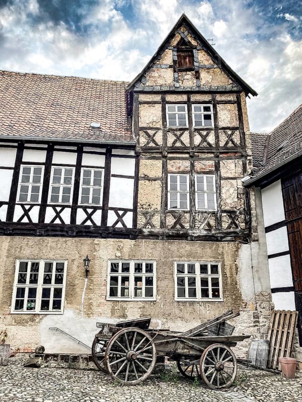 Part of west wing of historic aristocratic farm Fleischhof with restored 16th century half-timbered house, in front of it historic wooden carriage with spoked wheels, Quedlinburg, Harz, Saxony-Anhalt, Germany