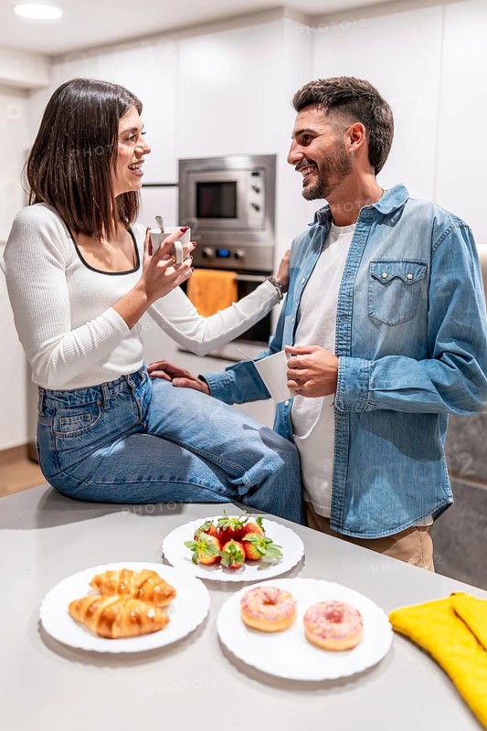 Young couple sharing a moment together over coffee, pastries, and strawberries in their contemporary kitchen
