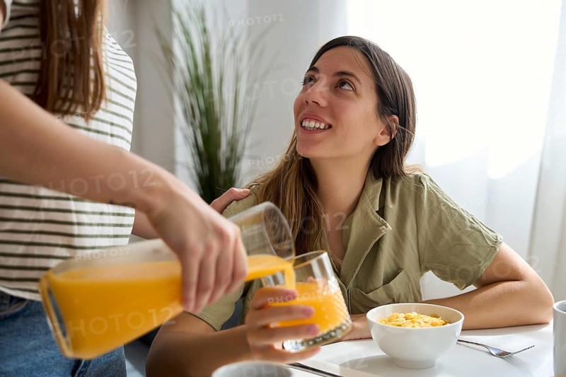 A lesbian couple enjoys a casual breakfast at home One woman smiles warmly as her partner pours fresh orange juice, creating a moment of connection and love