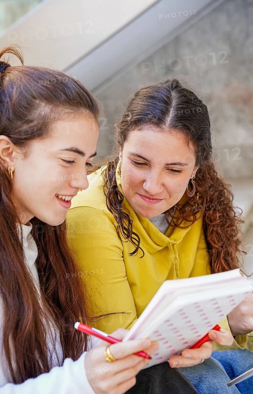 Two friends share a moment of study and collaboration, sitting closely while looking at a notebook Their lively conversation suggests teamwork and learning