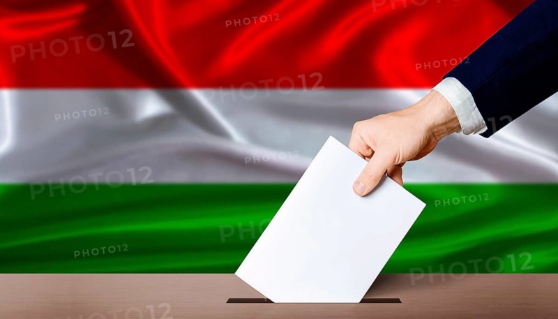 Hand placing a ballot in ballot box with the Hungarian flag in the background. Hungary parliamentary vote 2026