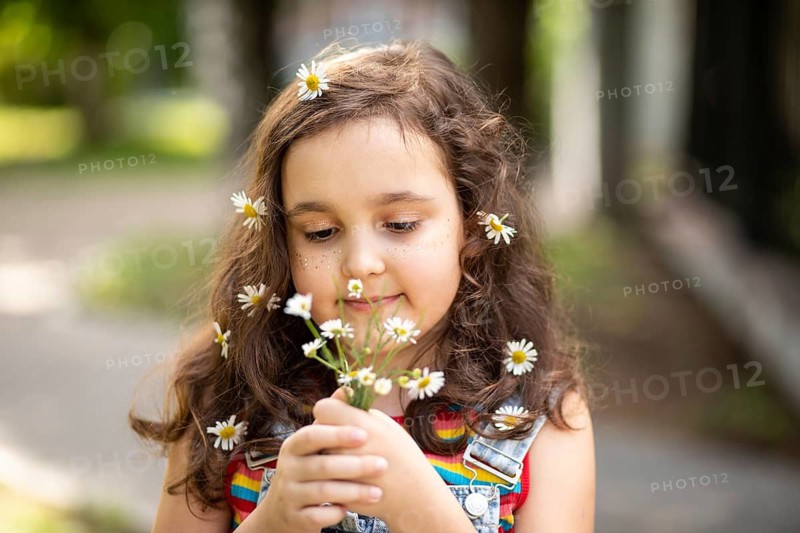 A joyful little girl in a rainbow-striped dress embraces the beauty of chamomile flowers. Her hair adorned with blooms, she embodies innocence and happiness in a sunny meadow