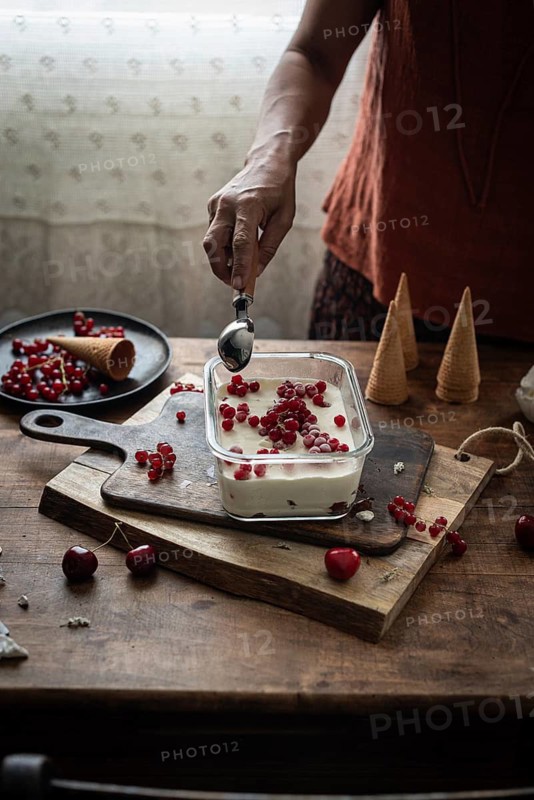 Cropped unrecognizable person scoops ice cream decorated with currants and gooseberries in a rustic kitchen setting