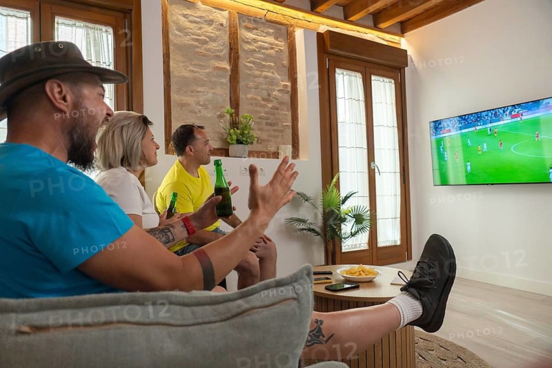Friends celebrating a scoring moment while watching soccer on television. Joyful reactions, casual lifestyle, friendship and sports entertainment at home