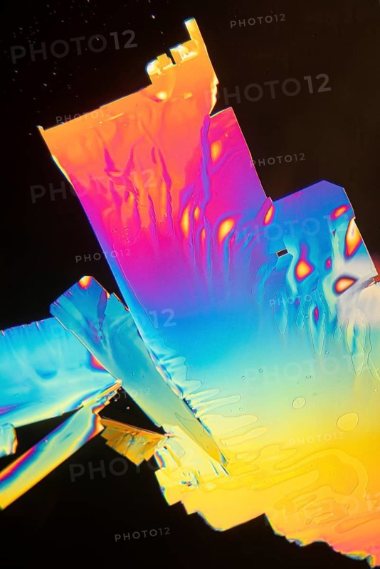 Microscopic view of Vitamin C crystals displaying a vibrant spectrum of colors, including pink, blue, orange, and yellow, against a dark background