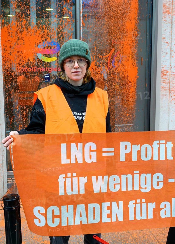 Regina Stephan, Last Generation activist after colour attack on Total Energies building. They are protesting against the World LNG Summit, which is due to take place in Berlin in December. The poster reads: LNG = profits for a few, harm for all!, Berlin, 6 November 2024