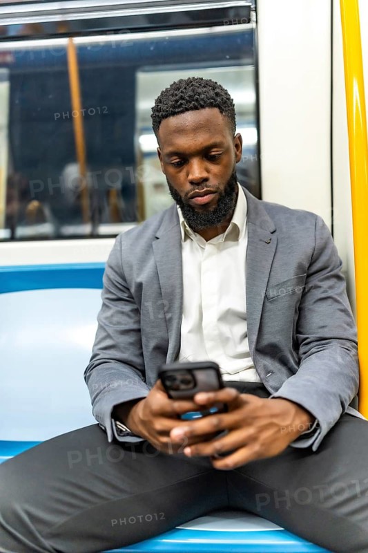 Young businessman sitting in a subway train, using a smartphone for browsing, checking emails, and staying connected while commuting