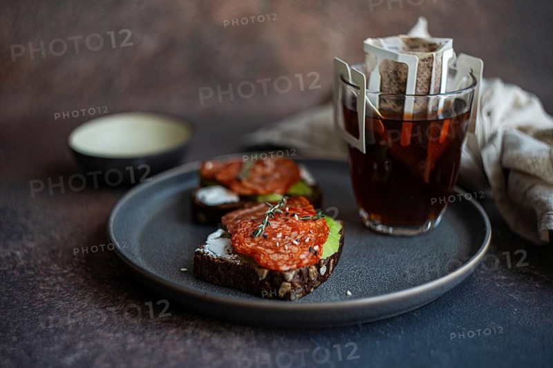 A visually appealing arrangement of whole wheat bread topped with savory pepperoni slices, served alongside a steaming cup of freshly brewed drip coffee for a perfect breakfast moment