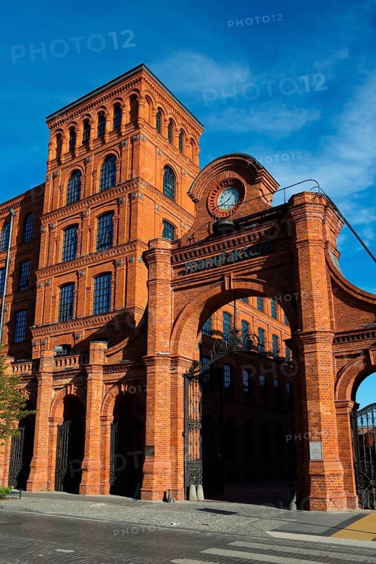 Impressive historic gate with clock and detailed brick structure under a blue sky, Manufaktura, Lódz, Lodz, Lodz, Poland