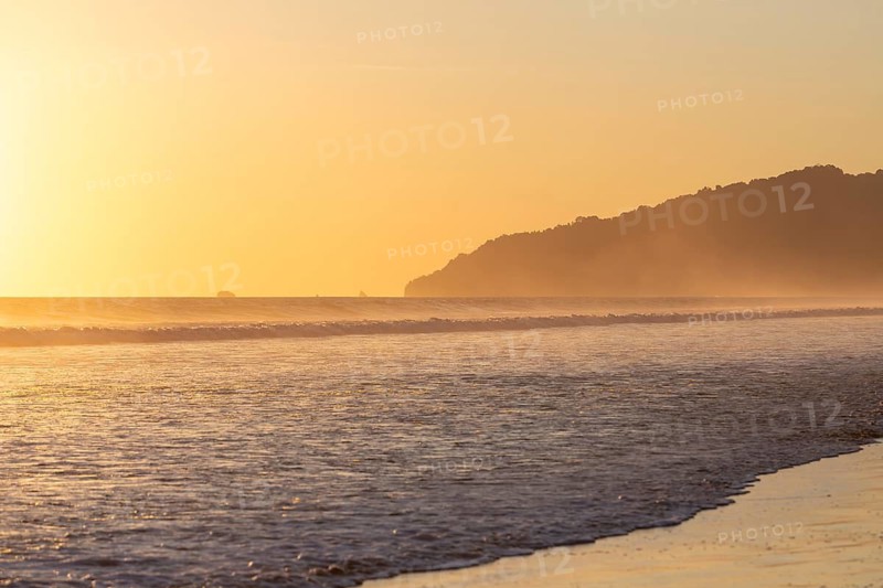 The low sun's golden light illuminates the ocean spray on Carate Beach, with views of Corcovado NP at sunset. Costa Rica