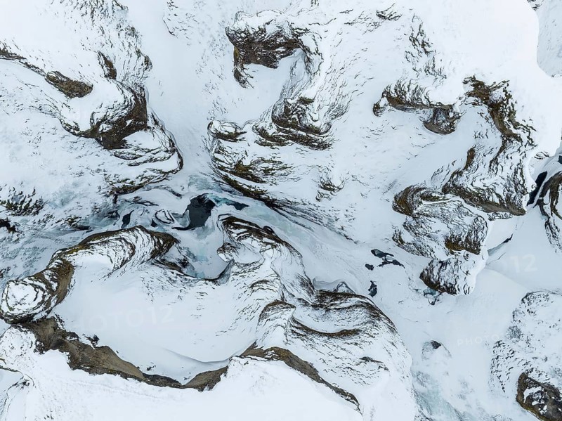 This aerial photo captures the abstract patterns of Iceland's snow-covered terrain, where rugged landforms contrast beautifully with soft white snow, offering a pristine winter scene