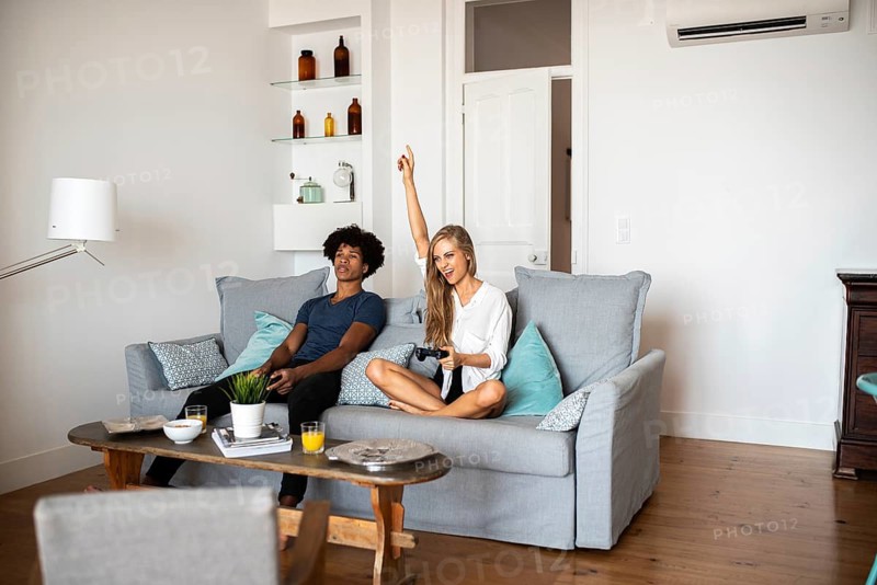Two friends share a moment on a comfortable sofa while playing a video game. One raises a hand in victory, symbolizing achievement and friendly competition in a relaxed living room setting