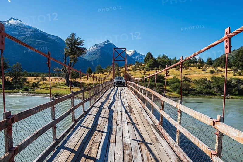 SUV driving over old-style orange suspension bridge, river Rio Nadis south of Cochrane, mountain range at Rio Baker in the back, Patagonia, Chile