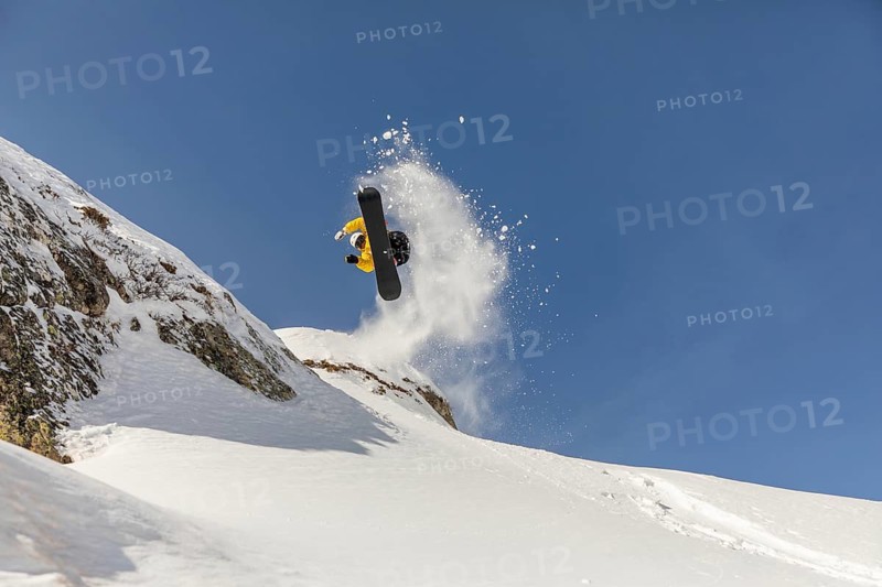 Thrilling image of a snowboarder executing a jump in the backcountry, surrounded by pristine mountain snow. A perfect depiction of winter freeride sport adventure