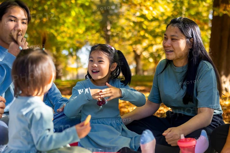A joyful Asian family enjoys a picnic in a lush, autumn park. Smiling faces and falling leaves create a warm, cheerful atmosphere in this seasonal outdoor gathering