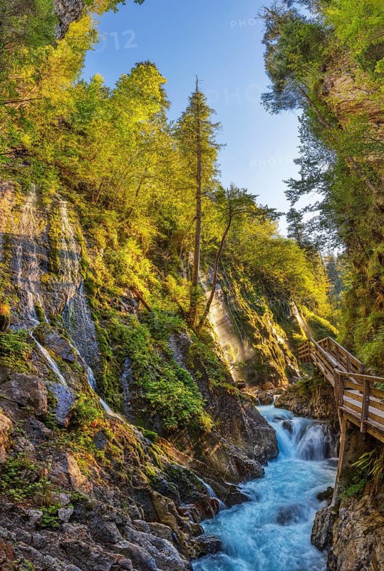 A sparkling waterfall in a sunlit gorge with a wooden bridge, Wimbachklamm gorge