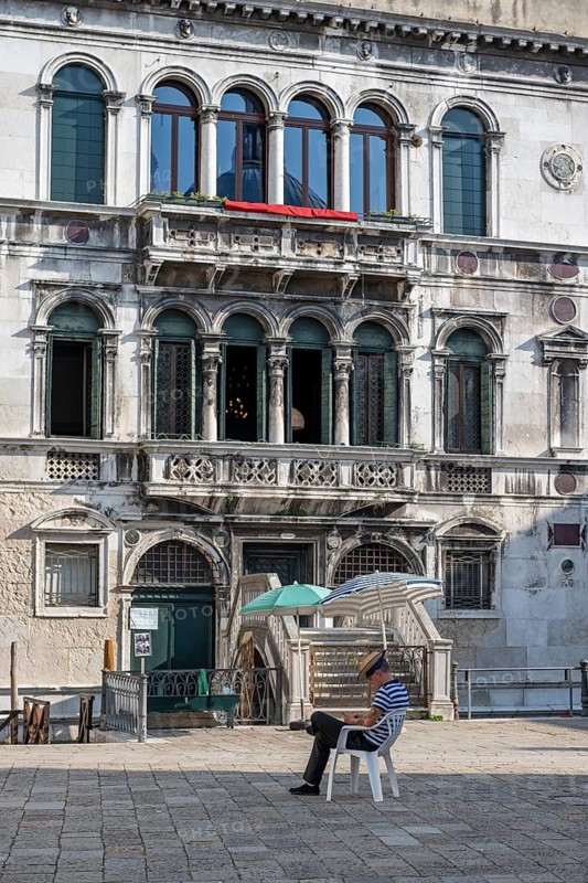 Gondolier sitting on a chair, waiting for customers, Venice, Italy