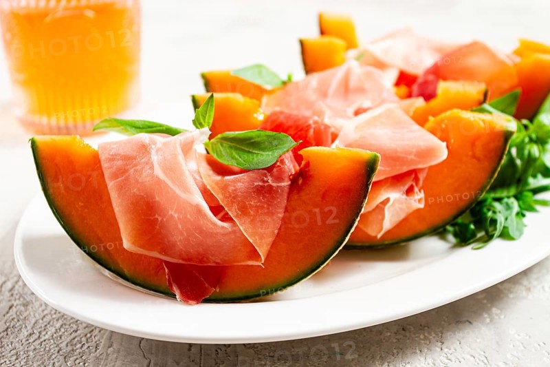 Cantaloupe melon with prosciutto and fresh basil, on a white plate, natural light