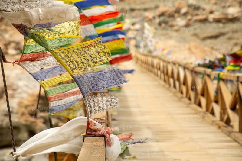 Vibrant prayer flags flutter on a wooden bridge near Phugtal Gompa in Ladakh, India. This serene scene captures the spirituality and cultural richness of the region
