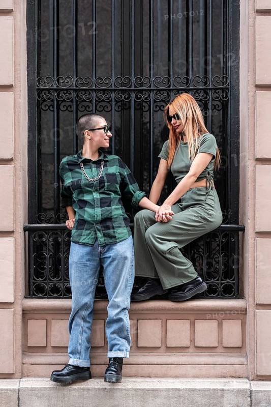 A Colombian lesbian couple sits together, holding hands and sharing a moment of love and connection, representing LGBTQIA+ unity and diversity against a city backdrop
