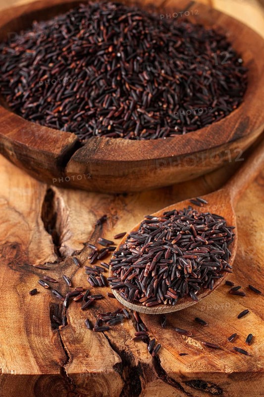 Natural black rice in a wooden bowl and spoon on a wooden surface in rustic style, top view