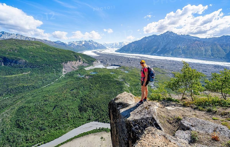 Young woman on a rocky outcrop enjoying the view, view of impressive mountain landscape with Matanuska glacier and glaciated mountain peaks, Lion's Head, Chugach Mountains, Alaska, USA
