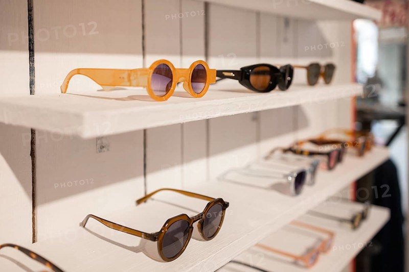 A variety of stylish sunglasses displayed on neatly arranged white shelves in a trendy store setting. Each pair showcases unique designs, reflecting current fashion trends