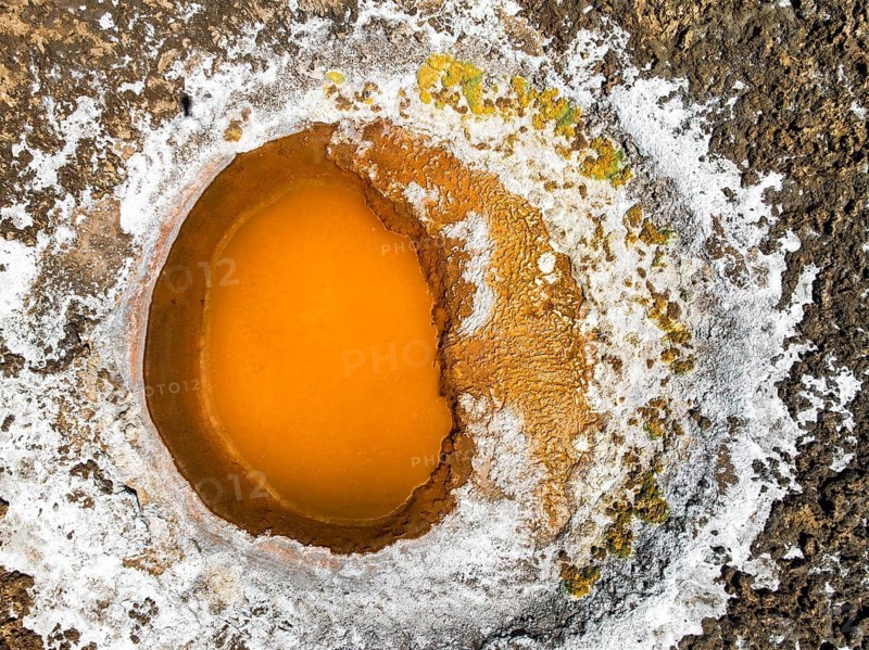 Top view of a vibrant geothermal pool nestled in the Salar de Antofalla, Catamarca, Argentina. The aerial image captures the contrasting colors and textures of this unique salt flat feature, uniquely to the Andean landscape