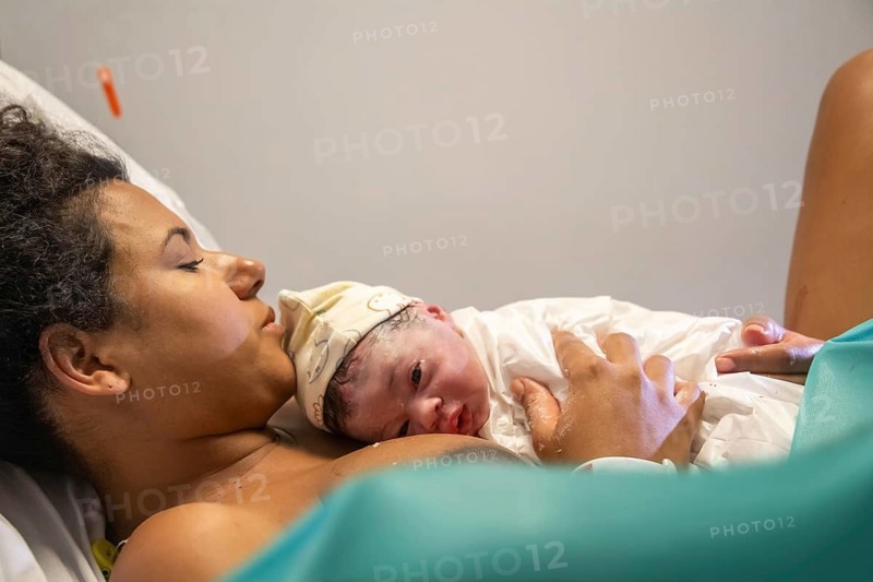 A tender moment between a mother and her newborn baby shortly after birth. The baby rests on the mother's chest, emphasizing the warmth and bond of early motherhood
