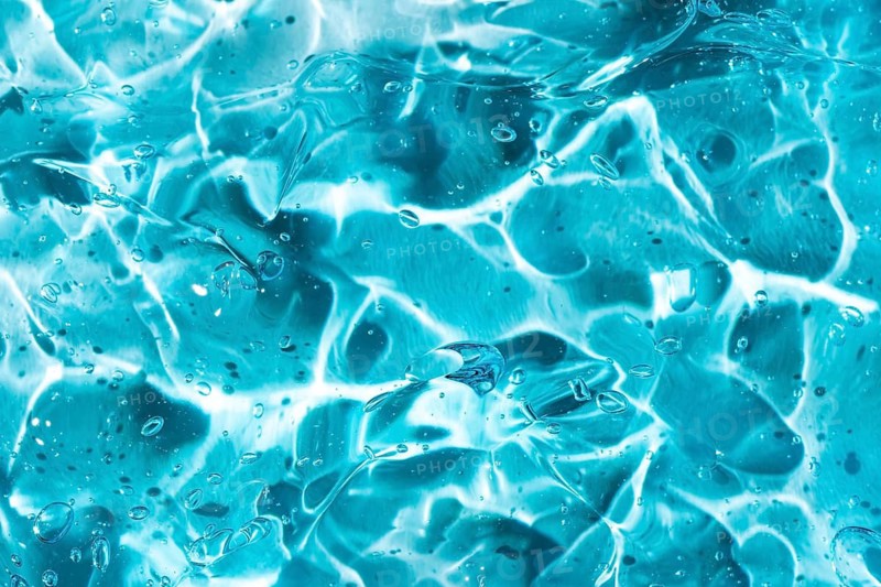 Close-up of a blue gel showcasing abstract fluid patterns and textures. The smooth surface reflects light, creating a dynamic interplay of highlights and shadows