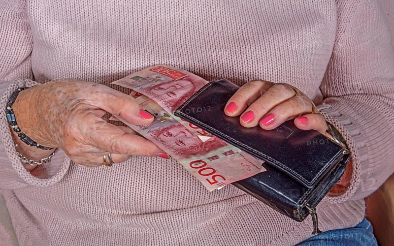 An elderly woman's hands take out Swedish banknotes from a wallet
