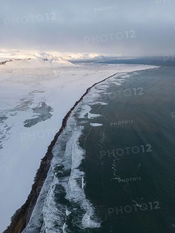 Aerial view of an Icelandic winter landscape, showcasing a stunning coastline with snow-covered terrain and waves crashing on the shore. The wild, remote beauty of Iceland, SnÃ¦fellsbÃ¦r, Vesturland, Islandia