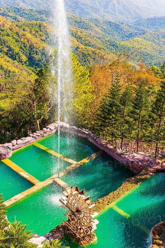 Turquoise green pond with fountain and water feature in the Wat Phra That Sorn Kaew Buddhist temple complex park, Phetchabun province, Thailand