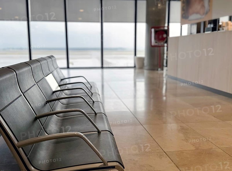 Empty airport seating area with metal benches, overlooking the tarmac through large windows. The floor is polished and reflects the serene, open space of the terminal