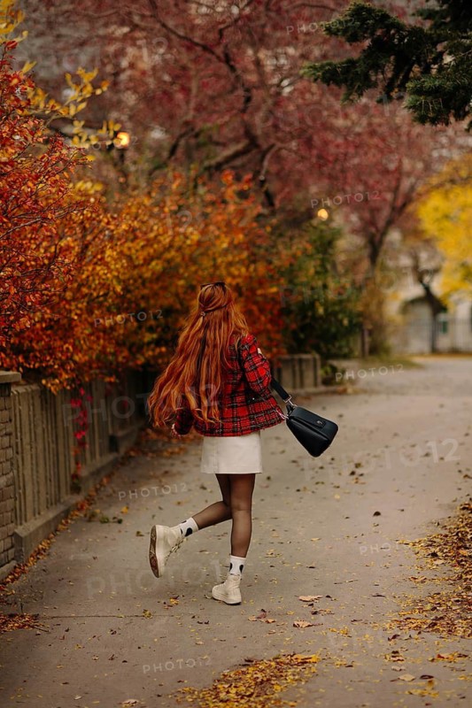 Back view of unrecognizable woman with red hair walking along a tree-lined path in Montreal. Fall leaves in vibrant colors create a beautiful backdrop in the urban setting