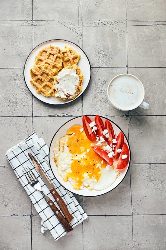 Top view of homemade breakfast or brunch. Fried egg with feta cheese and tomato, and belgian waffles with cream cheese. Cup of coffee drink