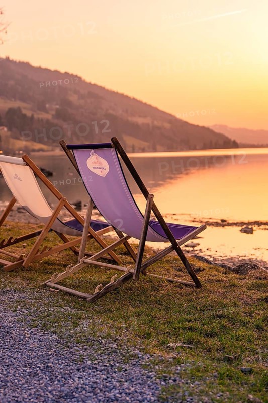Sun loungers on the shore of a lake at sunset, surrounded by mountains and peaceful atmosphere, Großer Alpsee, Immenstadt im Allgäu, Bavaria, Germany