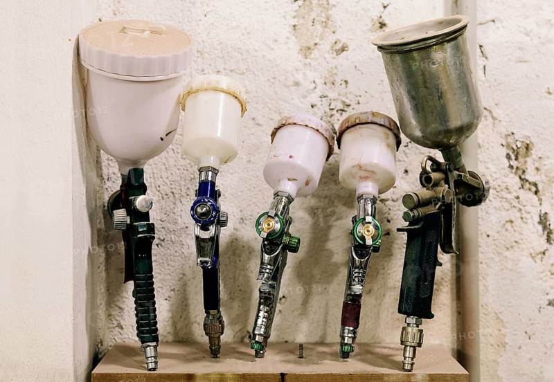 A collection of airbrushes and paint sprayers neatly arranged in a bass guitar luthier's workshop. Essential tools for detailed wood finishing and custom designs